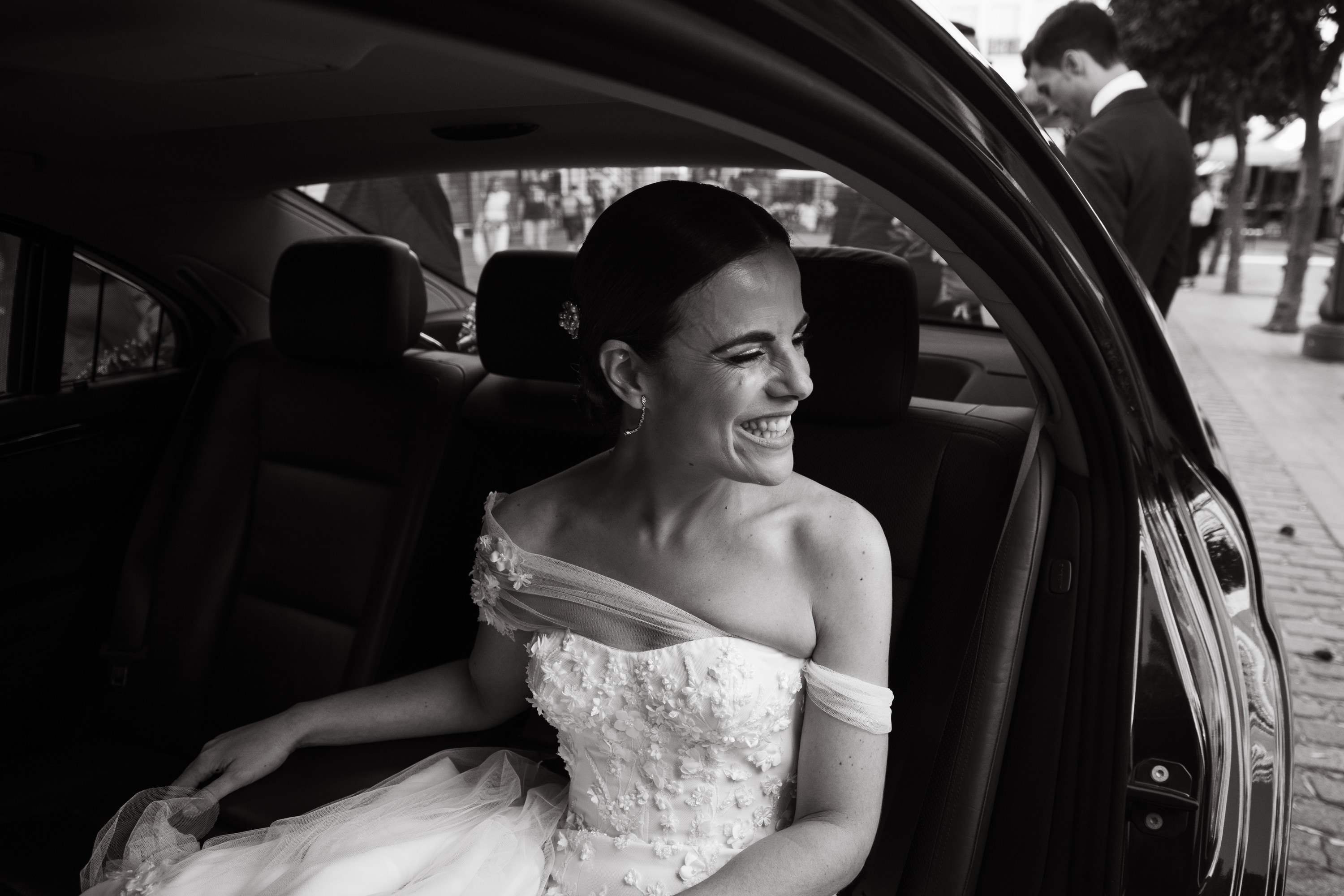 La novia ríe sentada en el coche, en blanco y negro, justo antes de salir hacia la ceremonia